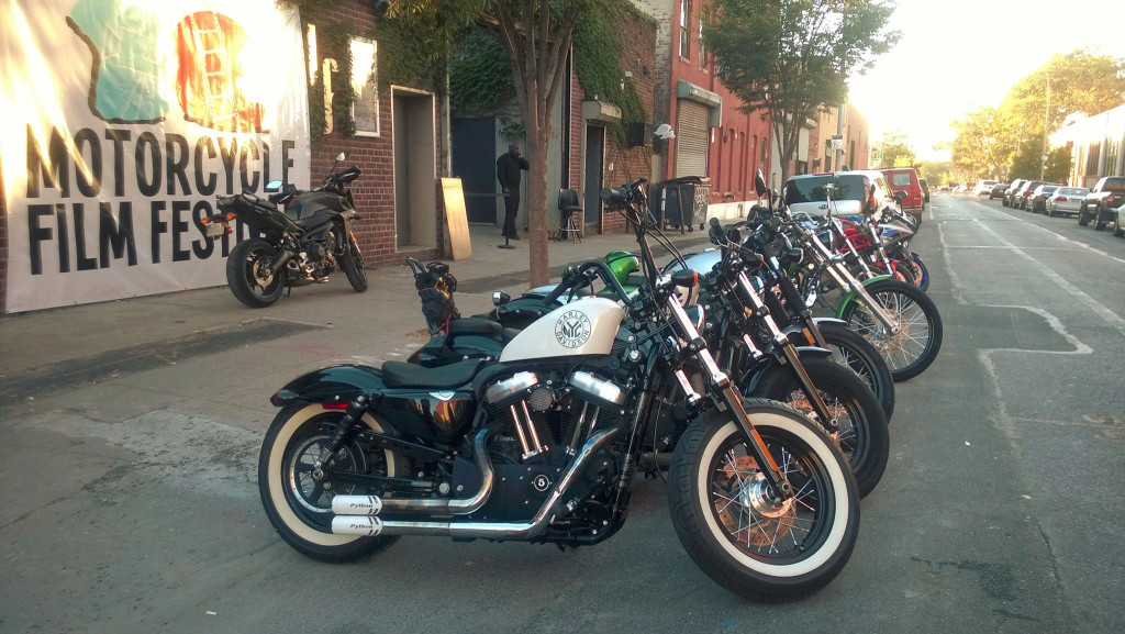 The 2015 Motorcycle Film Festival (Image depicts a row of motorcycles parked on the street in front of a building with a sign that says Motorcycle Film Festival)