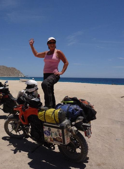 Women Who Ride: Sun, sand and surf - it doesn't get better than this! In Baja, Mexico Image shows a woman standing on a heavily loaded adventure motorcycle.
